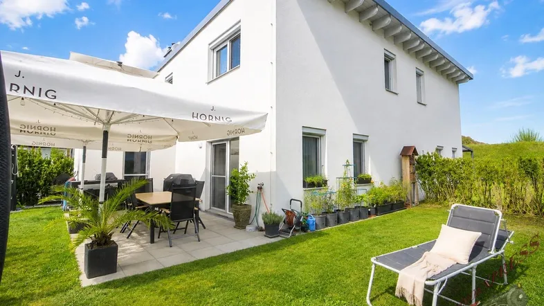 Große Terrasse mit Esstisch, Sonnenschirm und Liegestuhl im gepflegten Garten.