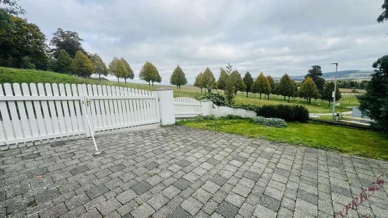 Gepflasterter Vorplatz mit weißem Zaun und weitem Blick über die hügelige Landschaft.