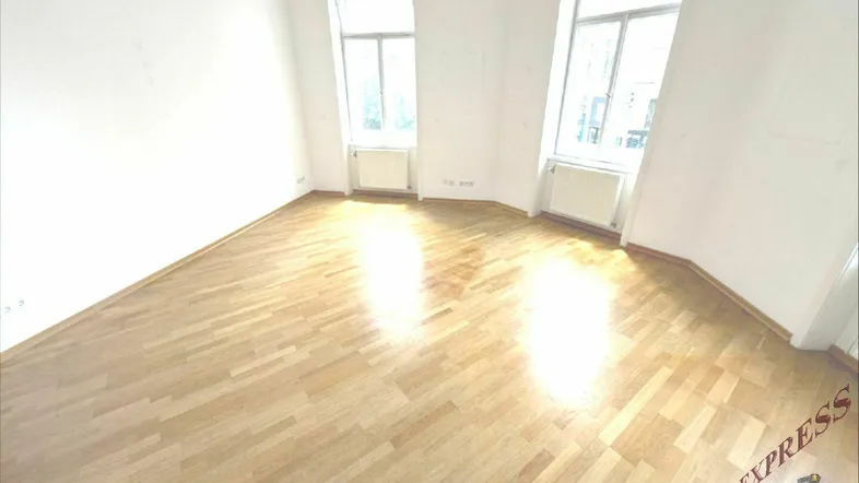 Heller Wohnraum mit Holzboden und großen Fenstern, die viel Tageslicht hereinlassen.