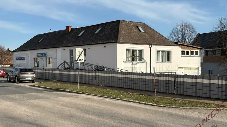 Ansicht des Gebäudes von der Straße mit einem Zaun und parkenden Autos davor.