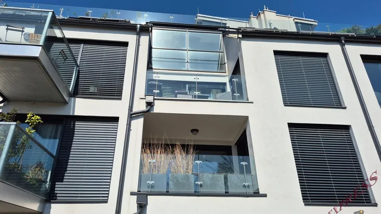 Moderne Fassade eines Neubaus mit Glasbalkonen und Jalousien unter blauem Himmel.