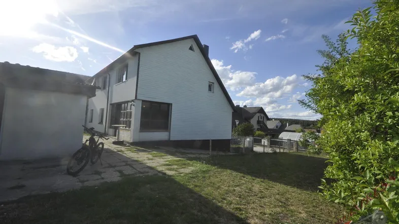 Seitenansicht des Hauses mit Rasenfläche und sonnigem Himmel, ein Fahrrad steht am Gebäude.