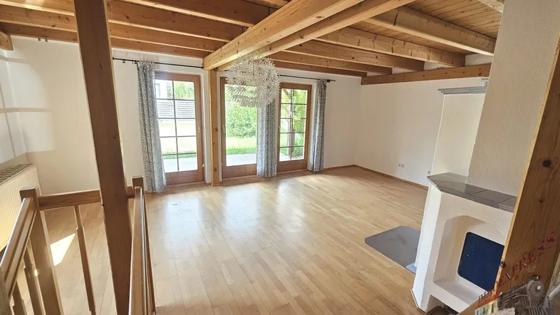 Helles Wohnzimmer mit Holzbalkendecke, Parkettboden und Kachelofen, mit Zugang zum Garten.