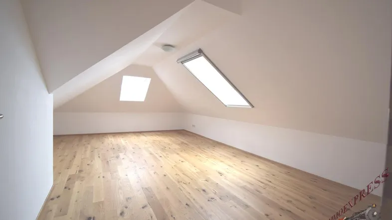Helles Dachzimmer mit Holzboden und zwei Dachfenstern, das viel Tageslicht hereinlässt.