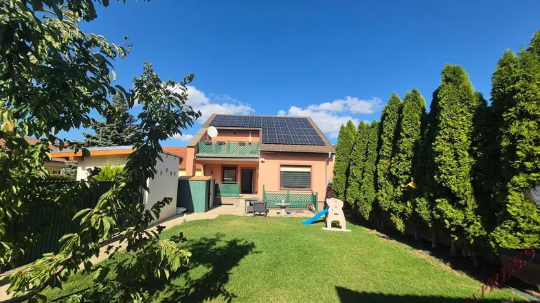 Großer Garten mit Rasenfläche, Spielgeräten und einer Terrasse hinter dem Haus unter blauem Himmel.