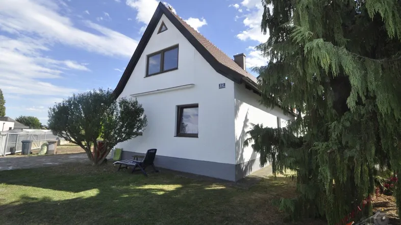 Freistehendes Einfamilienhaus mit weißer Fassade, Satteldach und gepflegtem Vorgartenbereich.