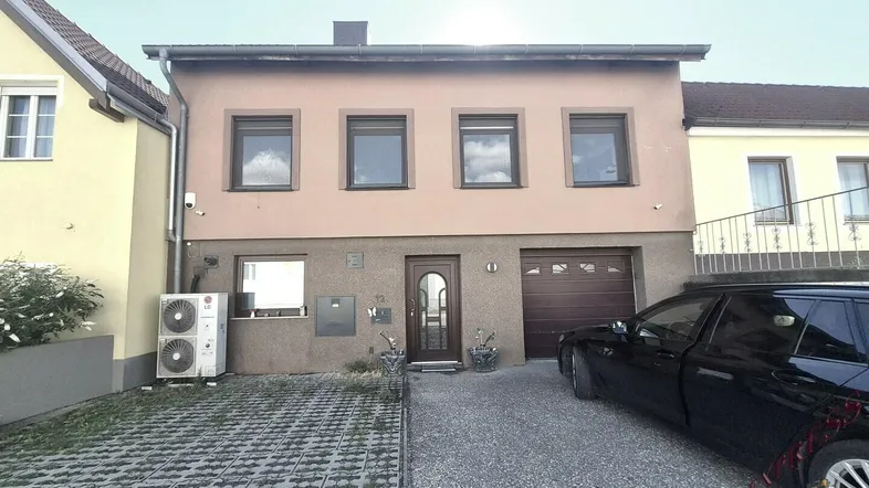 Frontansicht eines Einfamilienhauses mit Garage, Stellplatz und Wärmepumpe.