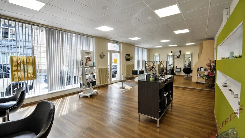 Geräumiger Friseursalon mit großen Fenstern, Holzfußboden und moderner Einrichtung.