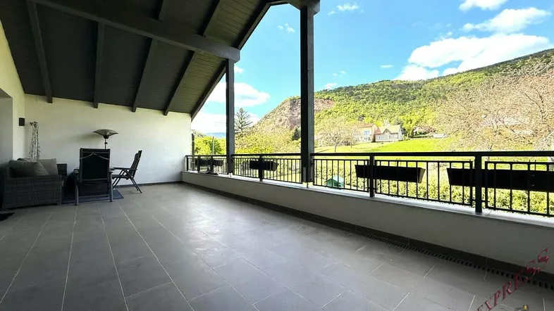 Große überdachte Terrasse mit Fliesenboden und Sitzgelegenheiten, bietet einen weiten Blick auf die umliegende Landschaft.