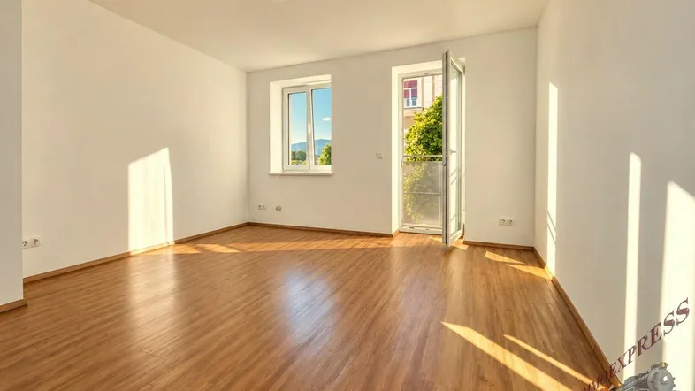 Helles, leeres Zimmer mit Laminatboden und Zugang zu einem französischen Balkon, durchflutet von Sonnenlicht.