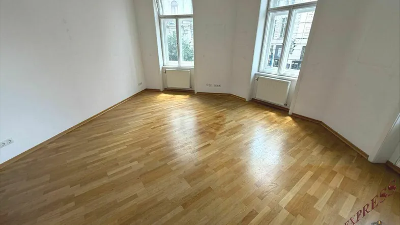 Helles Zimmer mit Parkettboden und hohen Fenstern, ideal als Wohn- oder Schlafbereich nutzbar.