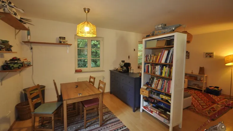 Gemütlicher Wohn- und Essbereich mit Holztisch, Bücherregal und Blick ins Grüne.