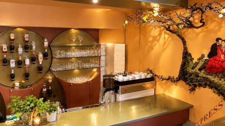 Gemütliche Bar mit goldener Theke, Kaffeemaschine und dekorativer Wandgestaltung, ideal für gesellige Abende.