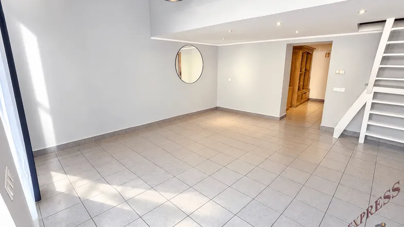 Geräumiger Wohnbereich mit hohen Decken, Fliesenboden und einer modernen Treppe zu einer oberen Ebene.