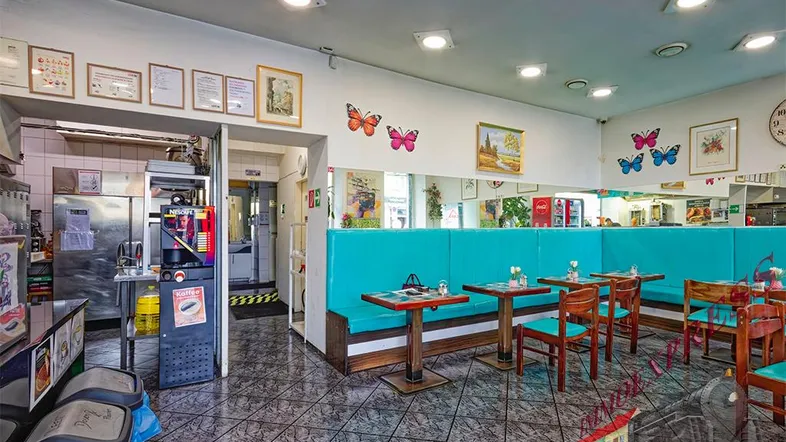 Gastraum eines Schnellrestaurants mit türkisfarbenen Sitzbänken, Tischen und Blick auf den Servicebereich.