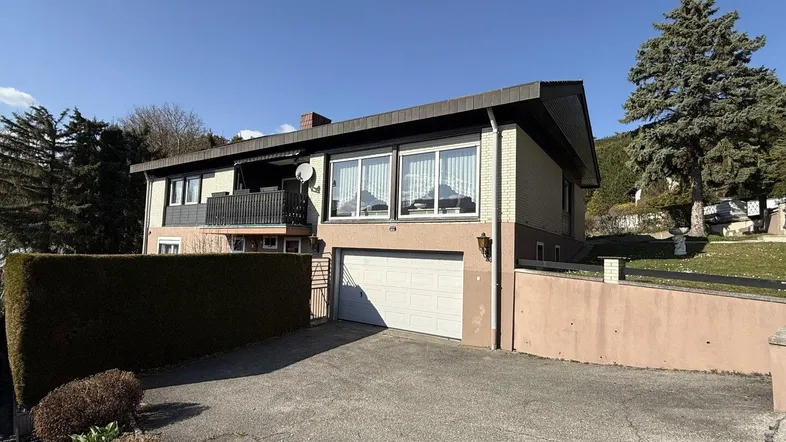 Ansicht des Hauses von vorne mit Garage, Einfahrt und Balkon im Obergeschoss.