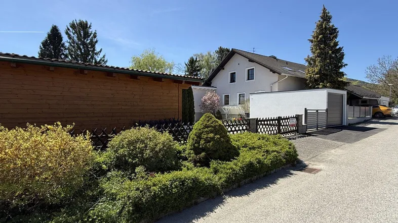 Ansicht des Hauses von der Straße mit Vorgarten, Zaun und einem Holzschuppen.