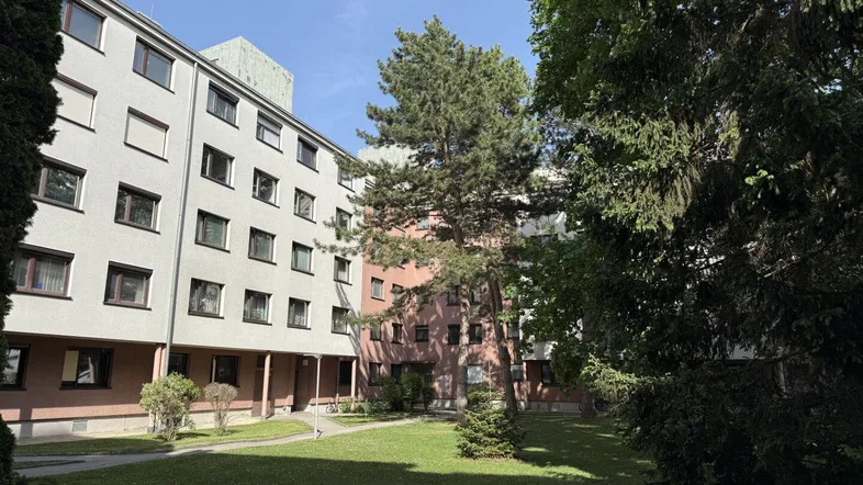 Wohngebäude mit mehreren Etagen und einem gepflegten grünen Innenhof unter blauem Himmel.