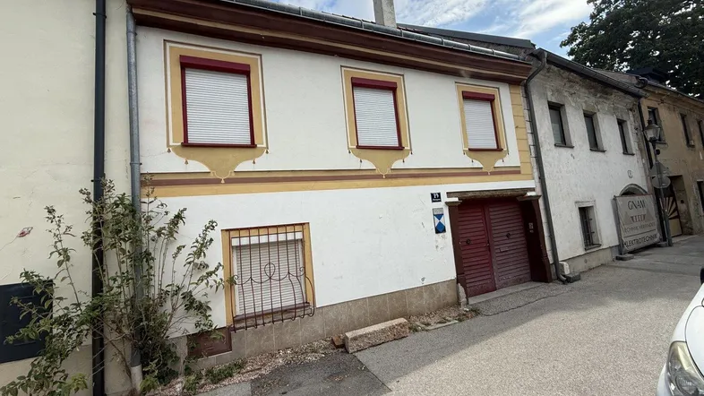 Altes Gebäude mit weißer Fassade, roten Fensterläden und dekorativen Elementen an einer Straße.