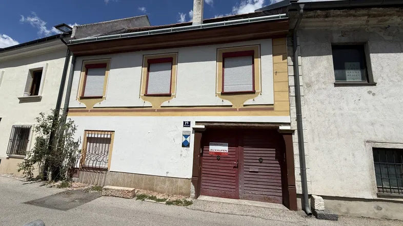 Fassade eines traditionellen Gebäudes mit Fensterläden und einem großen Holztor an der Straße.