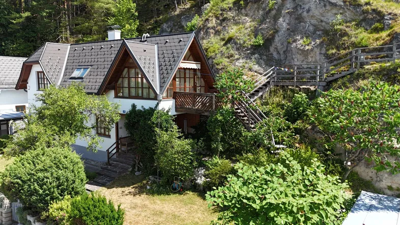 Charmantes Haus mit Satteldach und Balkon, eingebettet in eine grüne Hanglage mit viel Natur.