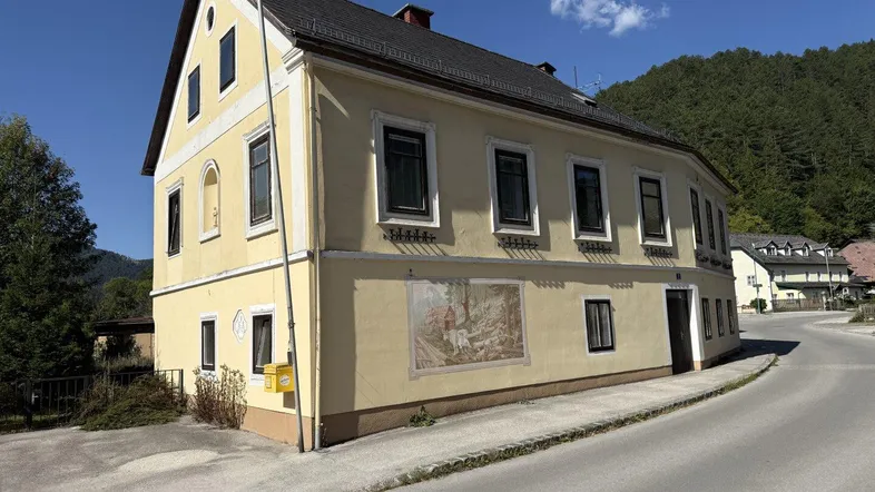Gelbes Gebäude mit Satteldach und traditioneller Fassadenmalerei an einer Straße.