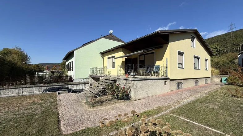 Gelbes Einfamilienhaus mit grünem Nachbargebäude und Garten in sonniger Umgebung.