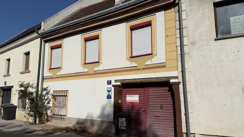 Historisches Gebäude mit weißer Fassade, gelben Verzierungen und roten Fensterläden unter blauem Himmel.