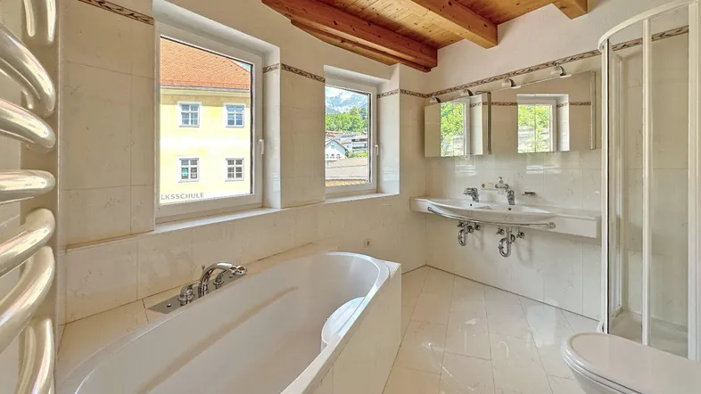 Helles Badezimmer mit Badewanne, Doppelwaschbecken, Dusche und Holzbalkendecke.