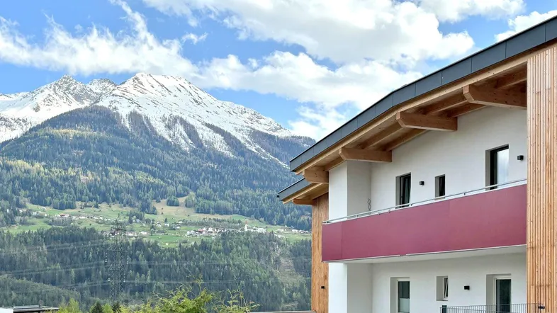 Modernes Gebäude mit Holzfassade und Balkonen, eingebettet in eine beeindruckende Berglandschaft.
