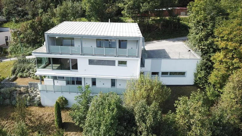 Moderne Architektur eines Mehrfamilienhauses in Hanglage, umgeben von üppiger grüner Vegetation.
