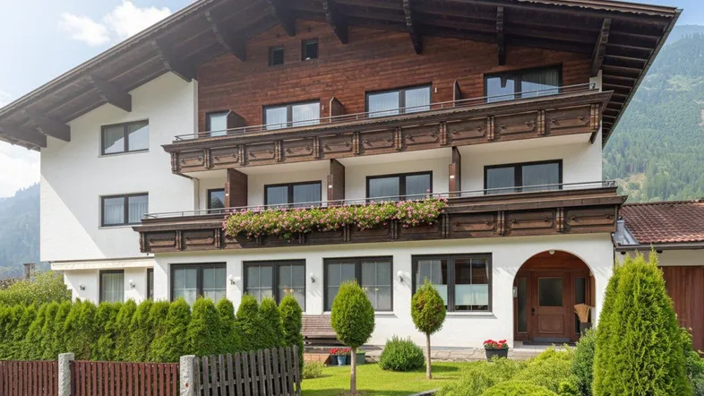 Traditionelles Haus im alpinen Stil mit Holzbalkonen, gepflegtem Vorgarten und Bergblick.