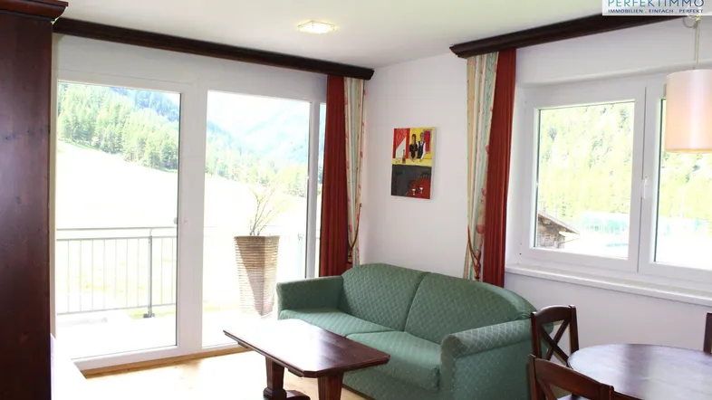 Heller Wohn- und Essbereich mit Bergblick, Zugang zum Balkon und gemütlicher Sitzecke.
