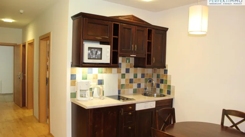 Kleine, funktionale Küche mit dunklen Holzschränken, heller Arbeitsplatte und Essbereich.