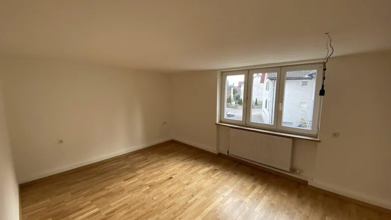 Helles Wohnzimmer mit Parkettboden, großen Fenstern und Blick nach draußen.