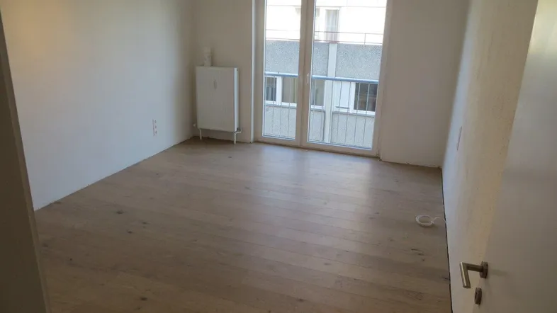 Heller Raum mit Holzboden und Zugang zu einem kleinen Balkon, ideal als Wohn- oder Schlafzimmer.