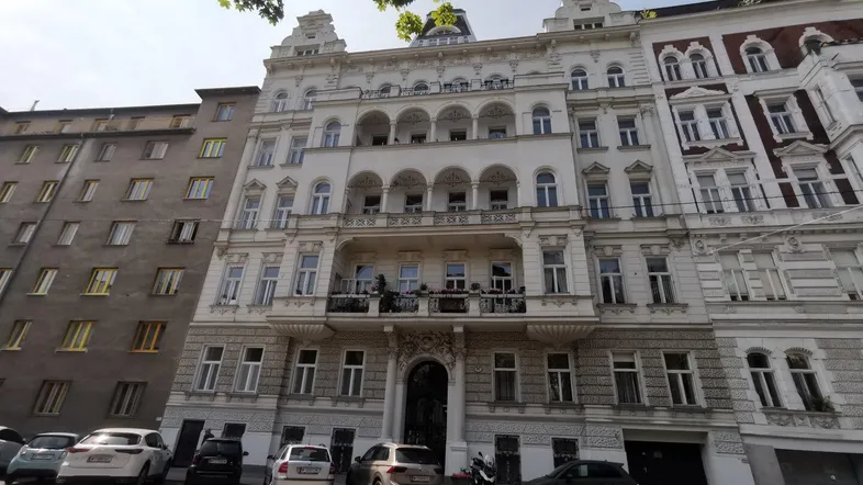 Historisches Mehrfamilienhaus mit reich verzierter Fassade und parkenden Autos auf der Straße.