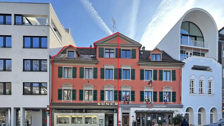 Historisches Gebäude mit roter Fassade, grünen Fensterläden und Geschäften im Erdgeschoss.