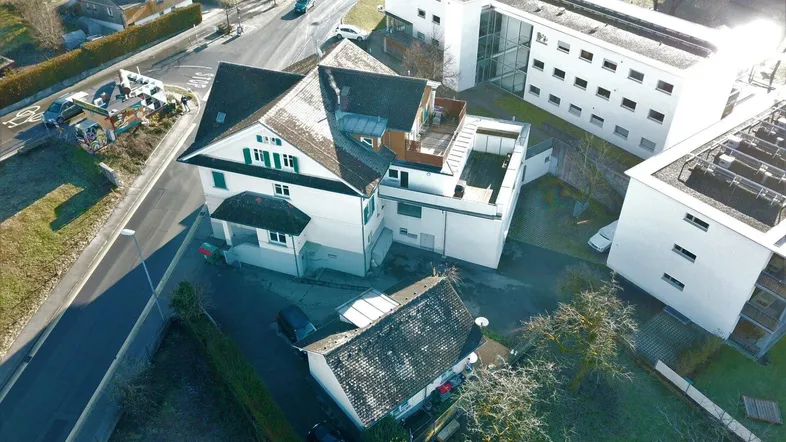 Luftaufnahme eines Gebäudekomplexes mit umliegenden Straßen und Grünflächen bei Tageslicht.