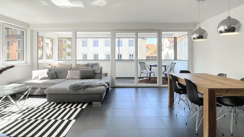 Heller Wohn- und Essbereich mit dunklen Fliesen, Zugang zum Balkon und moderner Einrichtung.