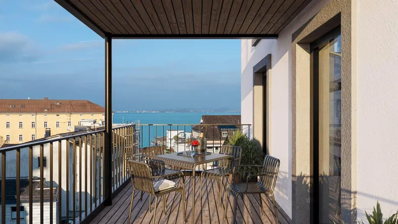 Geräumiger Balkon mit Holzboden und Sitzgelegenheiten, der einen weiten Blick auf den See bietet.