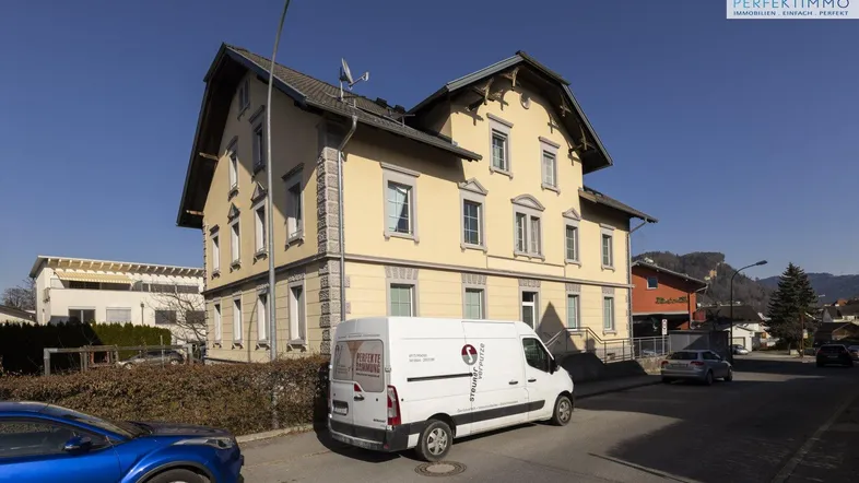 Traditionelles Gebäude mit gelber Fassade und Satteldach, an einer Straße gelegen.