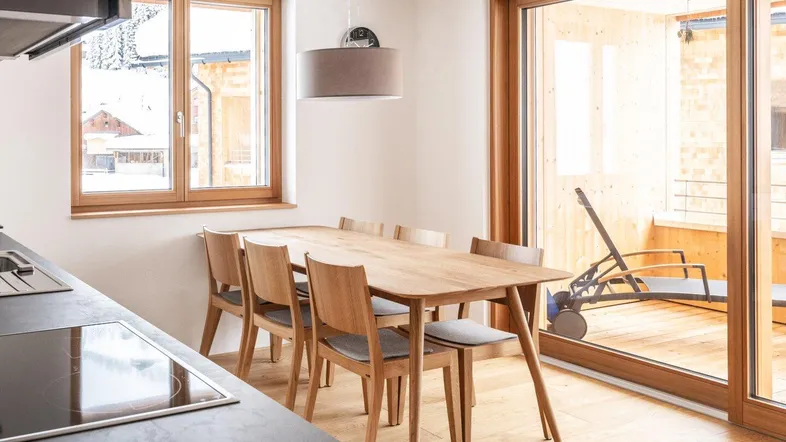 Moderne Küche mit Essbereich, Holzboden und Zugang zu einem sonnigen Balkon.