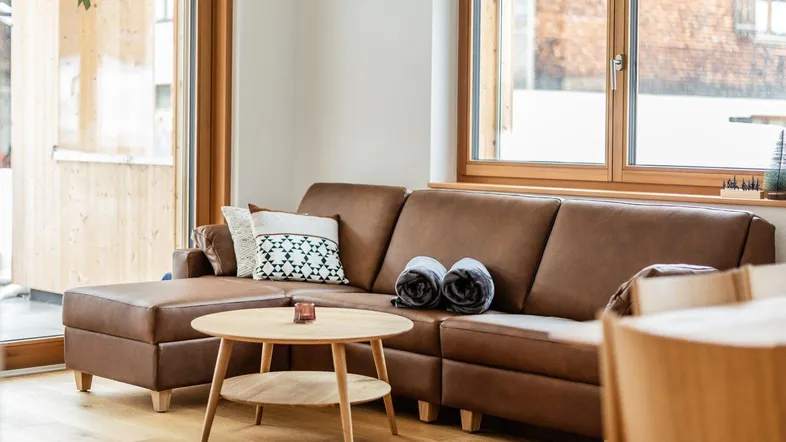 Gemütliches Wohnzimmer mit braunem Ledersofa, Holzboden und Zugang zu einem Außenbereich.