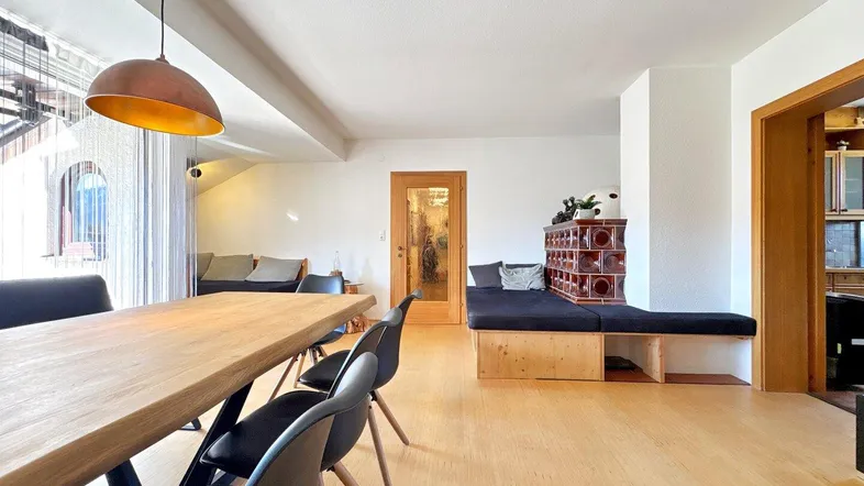 Geräumiger Wohn-Essbereich mit Holztisch, gemütlicher Sitzecke und traditionellem Kachelofen.