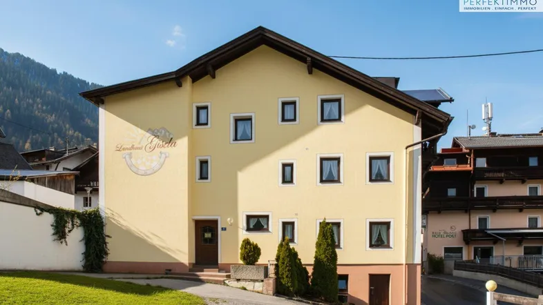 Traditionelles Landhaus mit gelber Fassade und Satteldach in alpiner Umgebung.