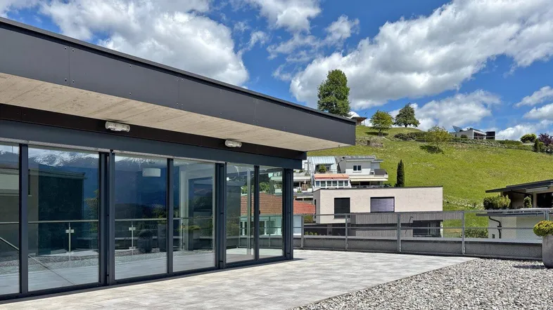 Große, gepflasterte Terrasse mit Glasfront und Blick auf die umliegende Berglandschaft.