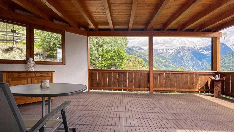 Große überdachte Terrasse mit Holzbalken und atemberaubendem Bergblick, ideal zum Entspannen.