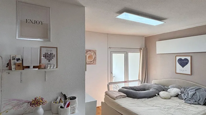 Helles Schlafzimmer mit großem Bett, moderner Deckenleuchte und Zugang zu einem Balkon.