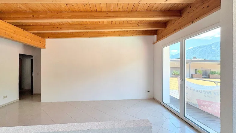 Heller Wohnraum mit Holzbalkendecke, Fliesenboden und großen Fenstern mit Bergblick.